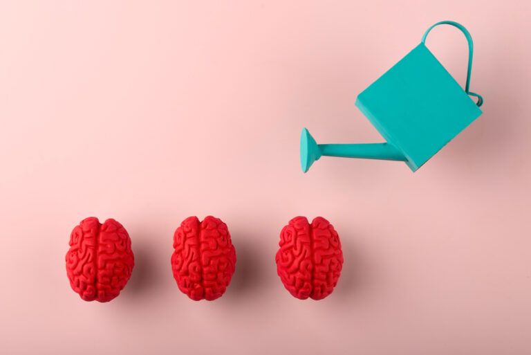 Drei rote Gehirne mit einer Gießkanne auf rosa Hintergrund symbolisieren Gesundheit.